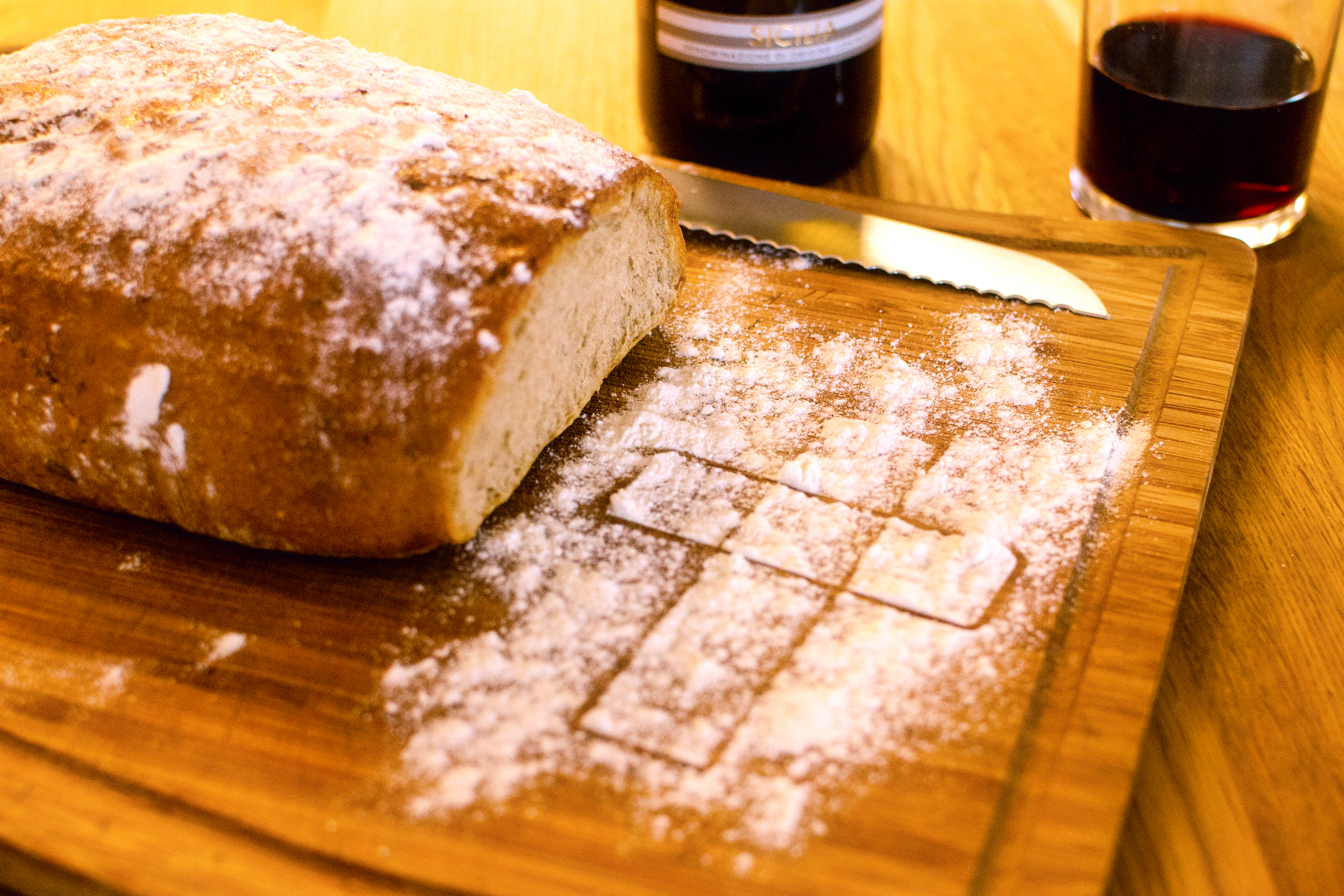 Bemehltes weiches Brot auf Schneidebrett, Abbbild des Dialogkreuzes im Mehl auf dem Schneidebrett. Im Hintergrund zwei Gläser mit Rotwein.