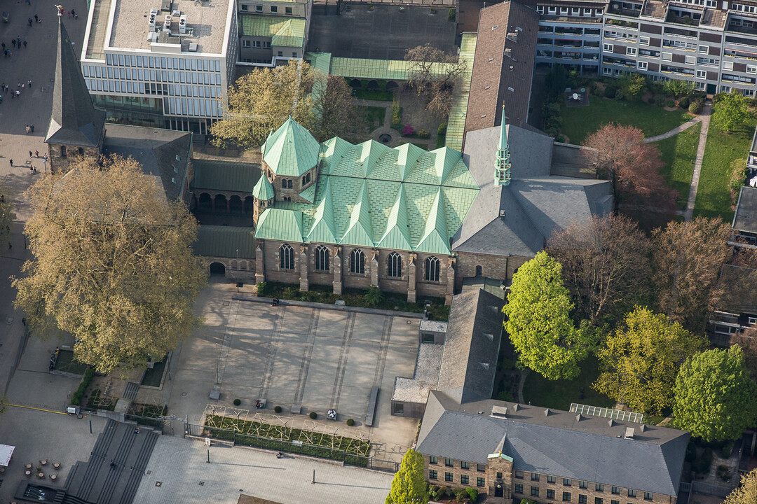 Blick auf den Dom von oben. Grünes gefaltenes Dach. Runterherum Bäume und Gebäude.